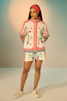 Woman wearing a ivory outfit set with a patterned shirt and shorts on a plain background