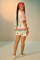 Woman wearing a ivory outfit set with a patterned shirt and shorts on a plain background