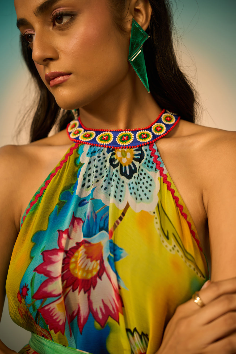 Close-up look of a woman modeling a sleeveless halter-neck midi dress with a vibrant multicolor floral and abstract print in shades of blue, green, yellow, and pink, styled with lime green pointed-toe heels against a studio backdrop.