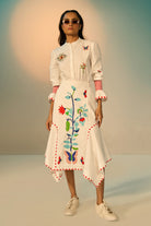 Woman wearing a ivory embroidered shirt with a skirt with colorful designs against a neutral background