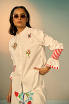 Woman wearing a ivory embroidered shirt with a skirt with colorful designs against a neutral background