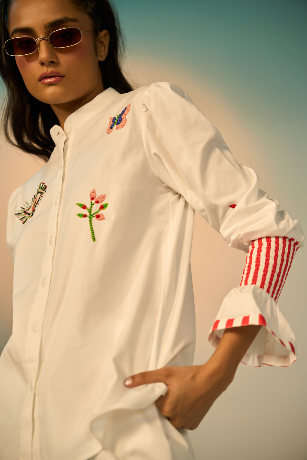 A close-up look of a woman wearing a ivory embroidered shirt with a skirt with colorful designs against a neutral background