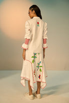 back view of a woman wearing a ivory embroidered shirt with a skirt with colorful designs against a neutral background