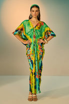 A woman modeling a vibrant, multicolored kaftan dress with a tie-dye pattern in multicolor, styled with a matching headband and gold accessories against a neutral studio backdrop.