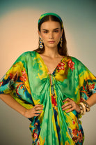 A close-up loof of woman modeling a vibrant, multicolored kaftan dress with a tie-dye pattern in multicolor, styled with a matching headband and gold accessories against a neutral studio backdrop.