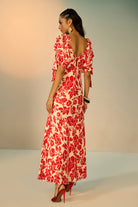 A woman modeling a red and cream floral print maxi dress with puff sleeves and a sweetheart neckline, standing against a neutral studio backdrop.