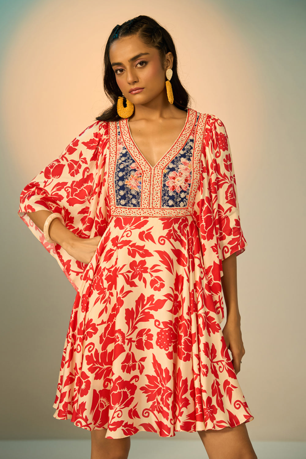A woman modeling a embroidered tunic with a red floral print on a cream background, featuring a navy blue embroidered yoke with redfloral details and a geometric border.