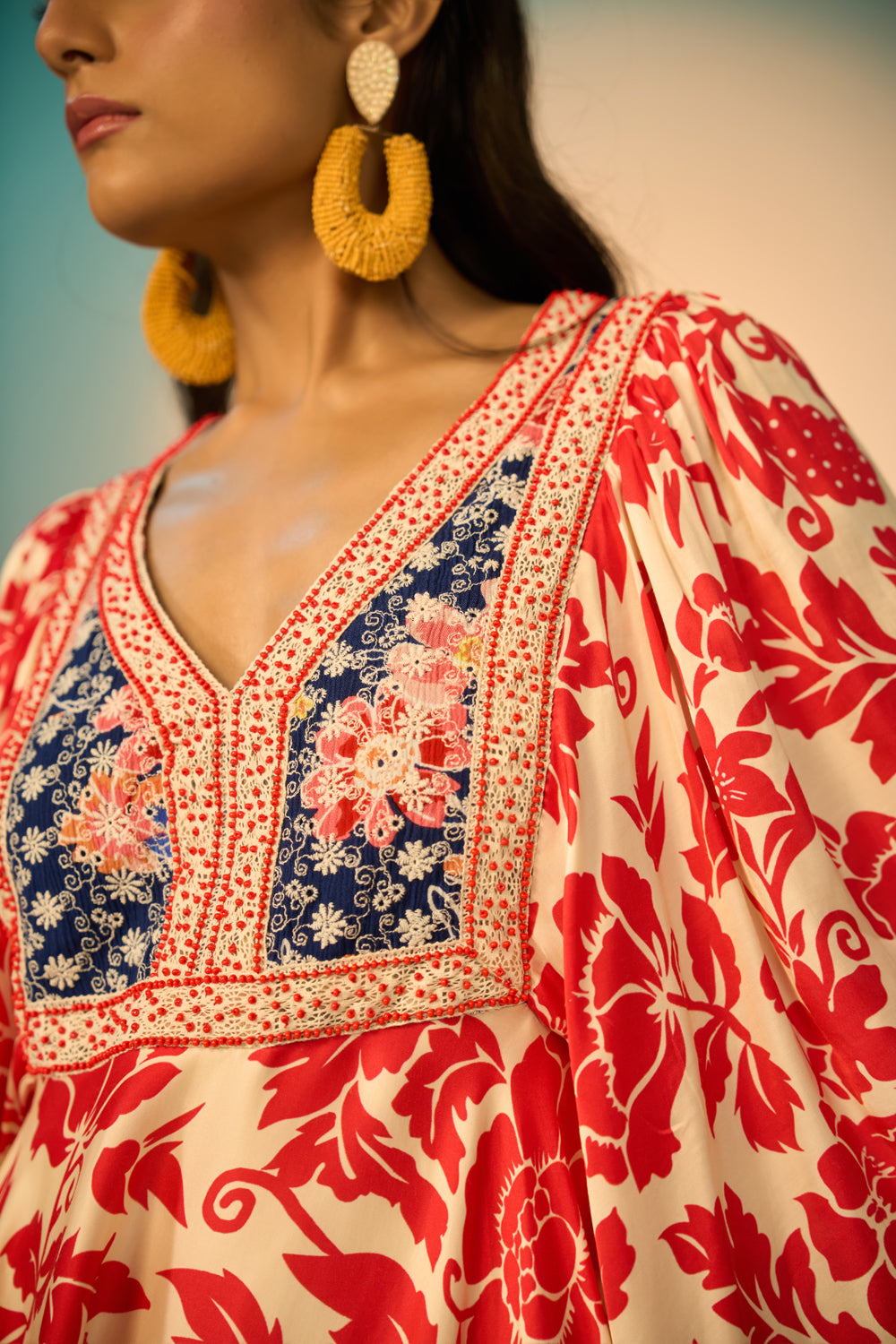 Close-up of a woman modeling a embroidered tunic with a red floral print on a cream background, featuring a navy blue embroidered yoke with redfloral details and a geometric border.