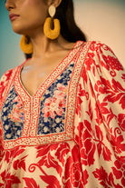 Close-up of a woman modeling a embroidered tunic with a red floral print on a cream background, featuring a navy blue embroidered yoke with redfloral details and a geometric border.