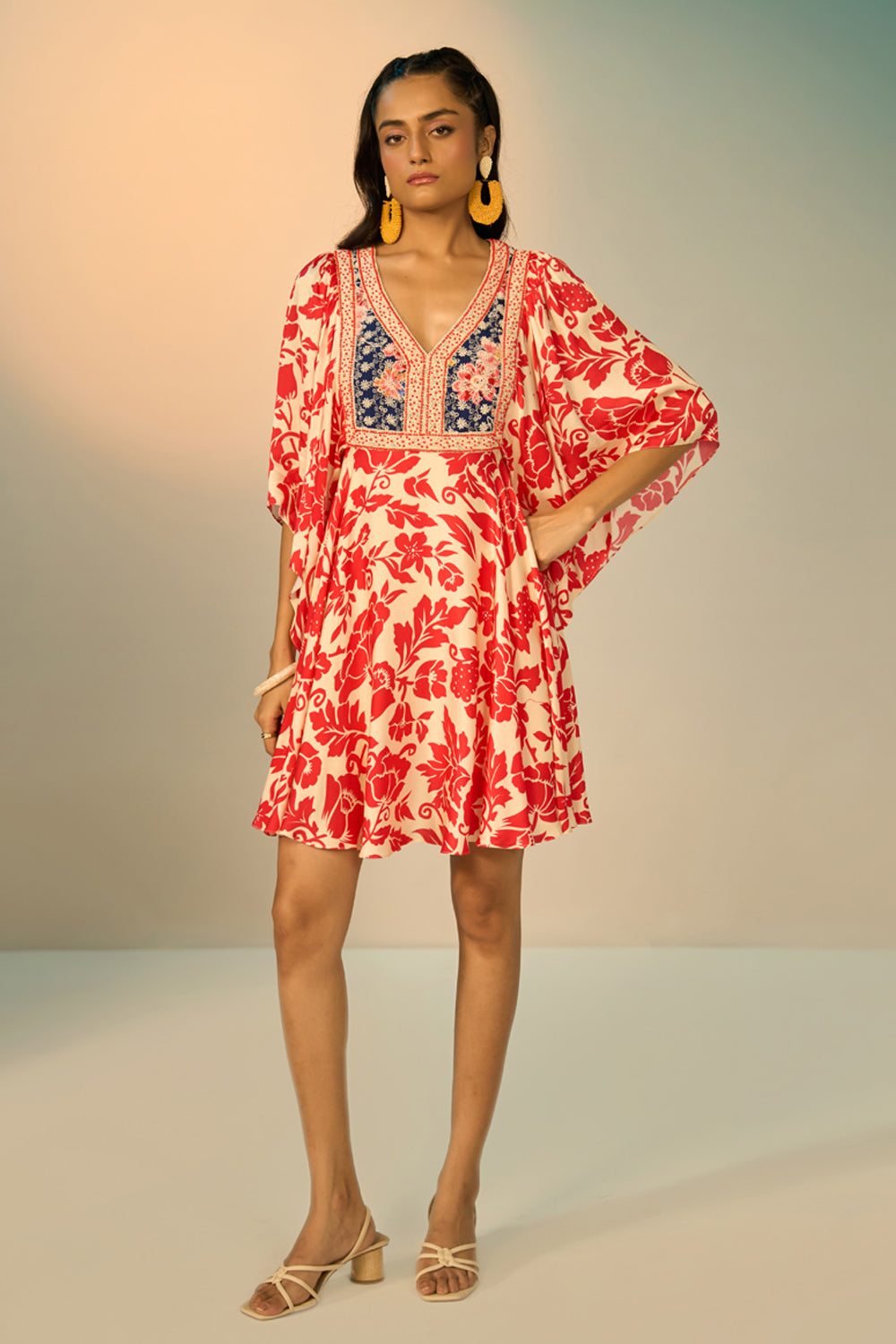 A woman modeling a embroidered tunic with a red floral print on a cream background, featuring a navy blue embroidered yoke with redfloral details and a geometric border.