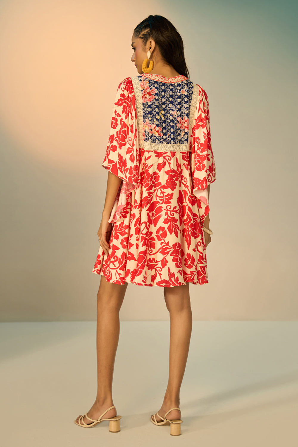 A woman modeling a embroidered tunic with a red floral print on a cream background, featuring a navy blue embroidered yoke with redfloral details and a geometric border.