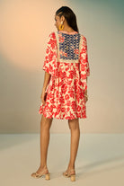 A woman modeling a embroidered tunic with a red floral print on a cream background, featuring a navy blue embroidered yoke with redfloral details and a geometric border.